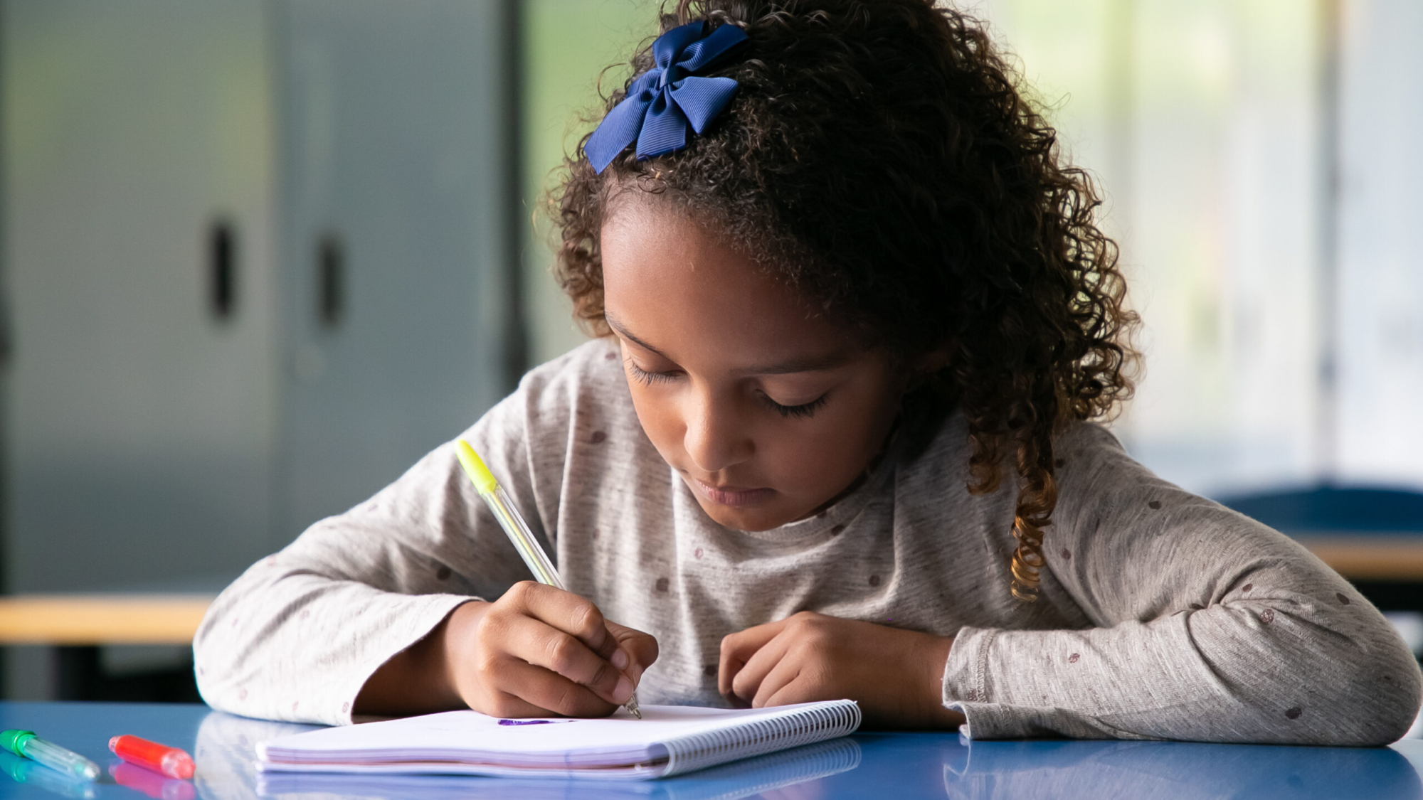 Focused mix raced girl sitting at school desk and drawing in copybook. Front view. Education or back to school concept