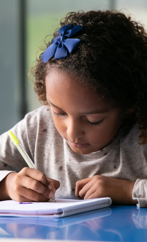 Focused mix raced girl sitting at school desk and drawing in copybook. Front view. Education or back to school concept